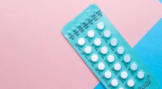 Eine Nahaufnahme einer türkisfarbenen Blisterpackung mit weißen Antibabypillen, die schräg auf einem zweifarbigen Hintergrund in Rosa und Blau liegt. Die Wochentage sind auf der Packung aufgedruckt. Das Bild symbolisiert die klassische hormonelle Verhütung im Vergleich zur natürlichen Zyklusbeobachtung mit trackle.