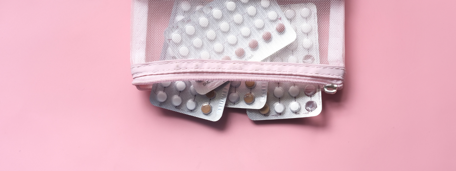 Eine Nahaufnahme von Blisterpackungen mit weißen Antibabypillen, die auf einem rosafarbigen Hintergrund liegen. Das Bild symbolisiert die klassische hormonelle Verhütung im Vergleich zur natürlichen Zyklusbeobachtung mit trackle.