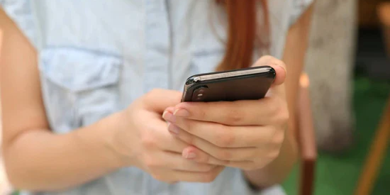 Eine Nahaufnahme der Hände einer Frau, die ein schwarzes Smartphone bedient. Sie trägt ein hellblaues Jeanshemd. Das Bild illustriert die Nutzung von Zyklus-Apps.