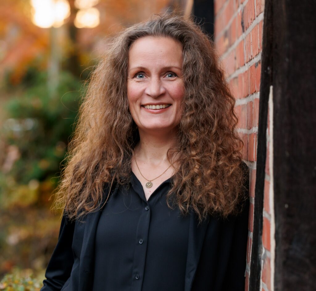 Porträt der Expertin Marthe Kniep. Sie lächelt freundlich und hat langes, lockiges Haar. Das Bild begleitet ein Interview zum Thema Partnerschaft und Beziehungen im Kontext der Zyklusbeobachtung mit trackle.
