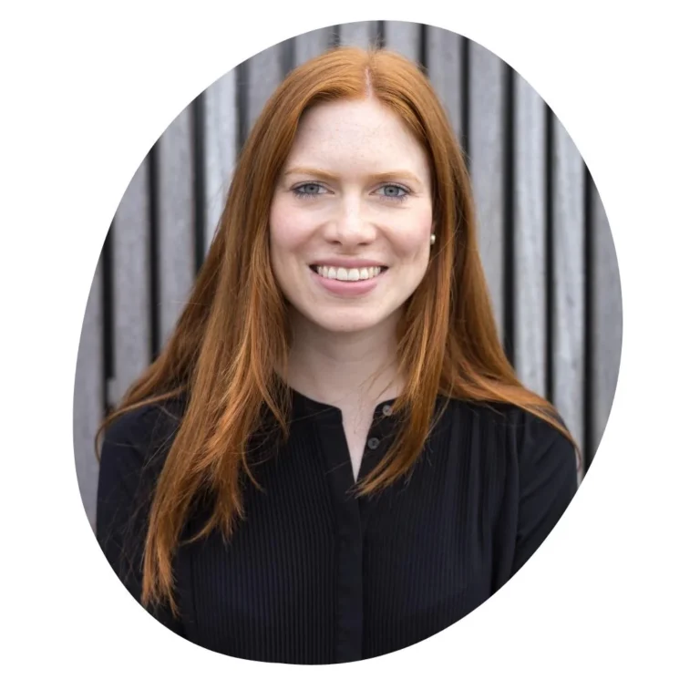 Ein kreisförmig zugeschnittenes Porträtfoto von Katharina Dinzen. Sie ist zertifizierte Expertin für NFP (Natürliche Familienplanung) & Zyklusgesundheit und Gründerin von Ovulista. Sie hat langes rotes Haar und lächelt sympathisch vor einem Hintergrund aus vertikalen grauen Holzlatten. Das Foto symbolisiert die Zusammenarbeit zwischen trackle und externen Fachkräften.