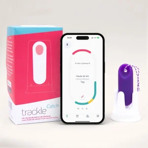 Das trackleCatch Sensorsystem in seiner Halterung neben der rot-blauen Originalverpackung und einem Smartphone, das die Zyklusphase in der App anzeigt.